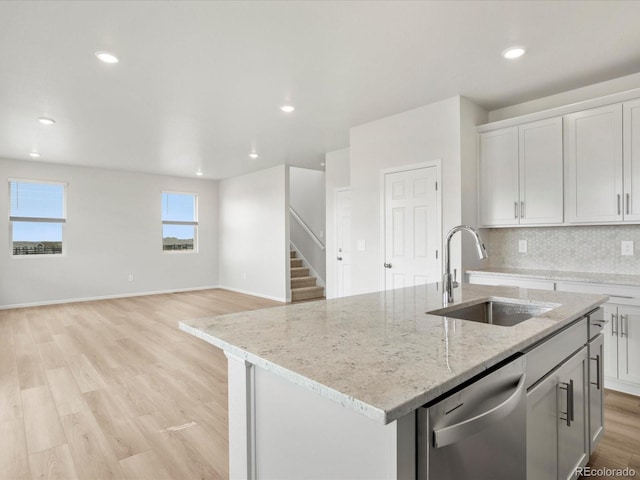 kitchen with a sink, dishwasher, light wood finished floors, tasteful backsplash, and an island with sink