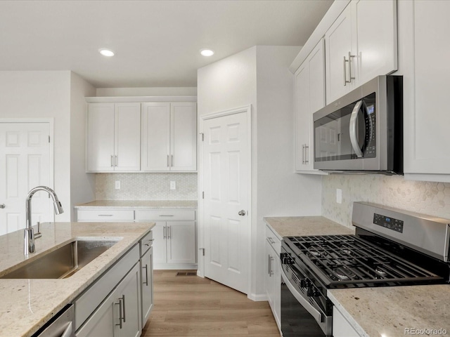 kitchen featuring stainless steel appliances, a sink, white cabinets, light wood-style flooring, and light stone countertops
