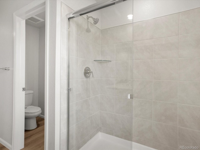 bathroom with a shower stall, toilet, and wood finished floors