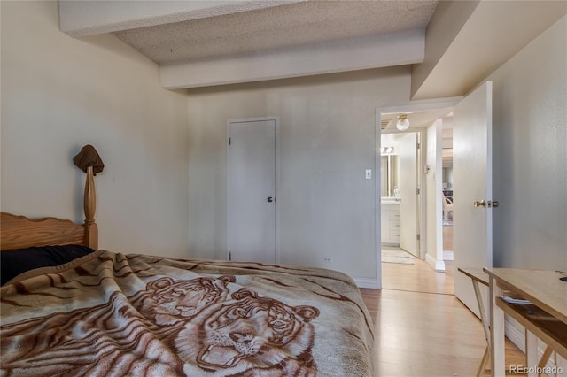 bedroom featuring a textured ceiling, light wood-type flooring, and beamed ceiling