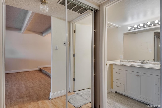 bathroom with a textured ceiling, hardwood / wood-style floors, and vanity with extensive cabinet space