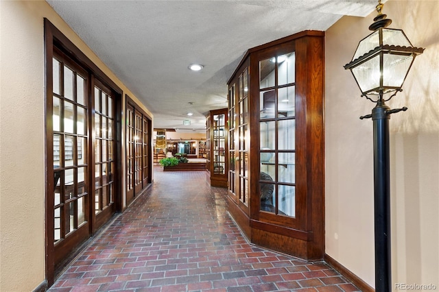 hallway featuring french doors, a textured ceiling, and a healthy amount of sunlight