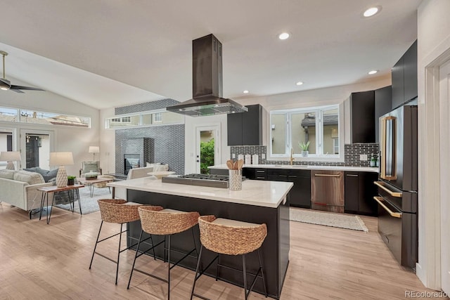 kitchen with island exhaust hood, stainless steel appliances, a kitchen breakfast bar, decorative backsplash, and a kitchen island