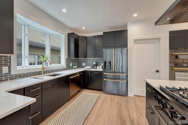 kitchen with stainless steel appliances, a sink, wall chimney range hood, decorative backsplash, and recessed lighting