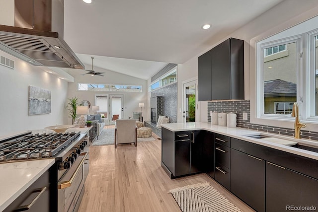 kitchen with high end range, exhaust hood, a sink, lofted ceiling, and light wood-style floors