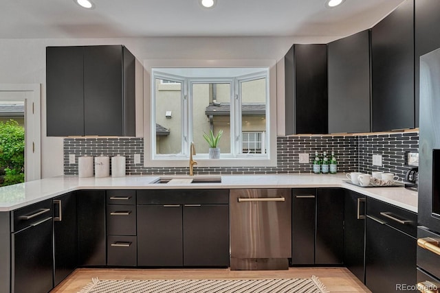 kitchen featuring dishwasher, a sink, light countertops, tasteful backsplash, and recessed lighting