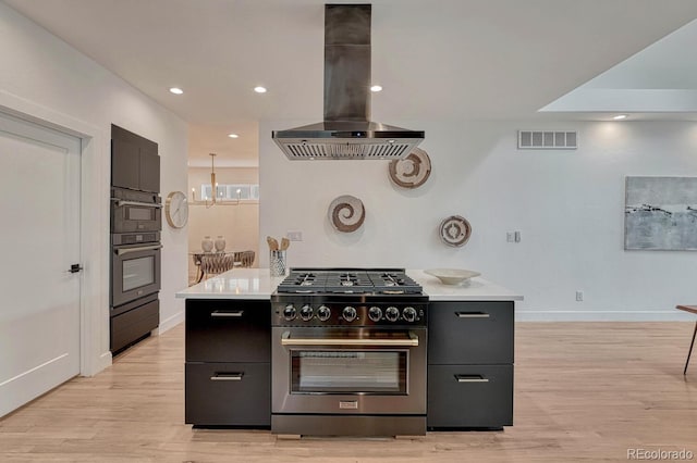 kitchen with stainless steel stove, island exhaust hood, dark cabinets, light countertops, and light wood-style flooring