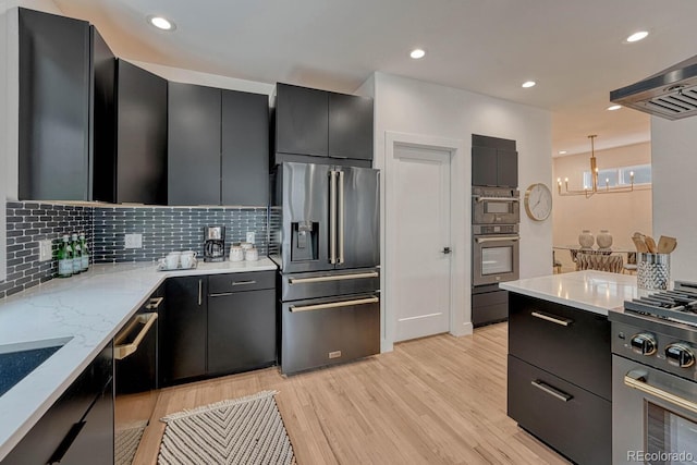 kitchen with appliances with stainless steel finishes, dark cabinetry, light wood-style floors, backsplash, and a chandelier