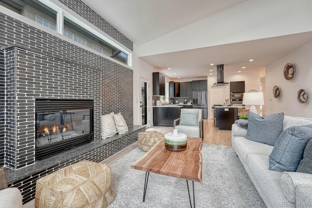 living area featuring a tile fireplace, light wood-style floors, lofted ceiling, and recessed lighting