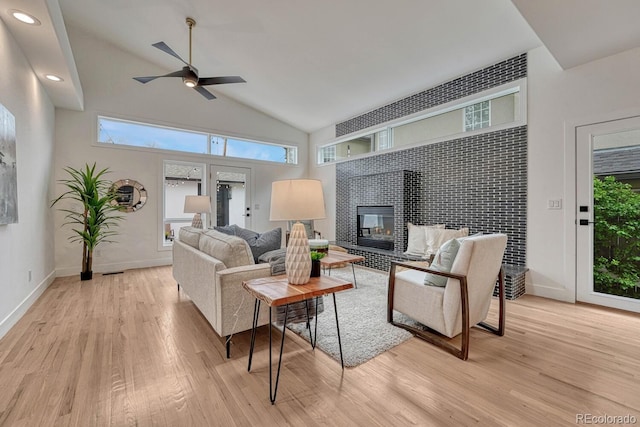 living area with light wood-style flooring, a ceiling fan, healthy amount of natural light, lofted ceiling, and a tiled fireplace