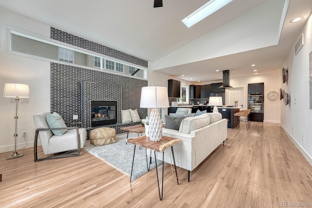living area with light wood-style floors, a tiled fireplace, baseboards, a skylight, and vaulted ceiling