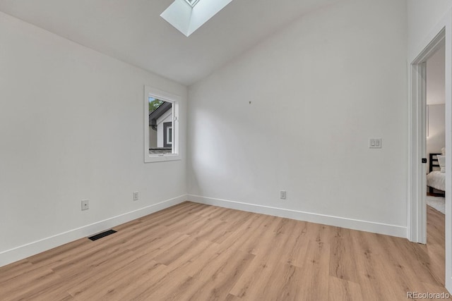 empty room with a skylight, light wood-style flooring, baseboards, and vaulted ceiling