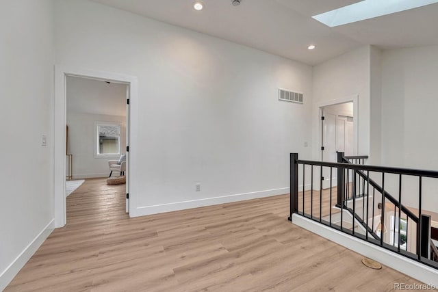 empty room featuring a skylight, light wood-style flooring, baseboards, and recessed lighting