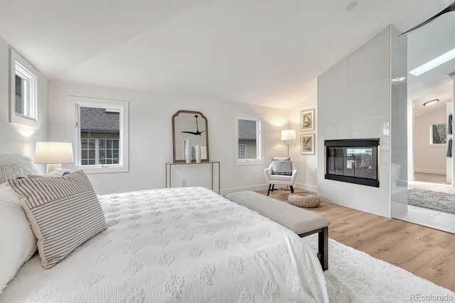 bedroom with vaulted ceiling, wood finished floors, a fireplace, and baseboards
