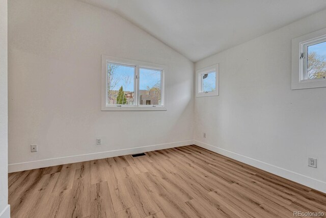spare room with light wood-style floors, baseboards, and vaulted ceiling