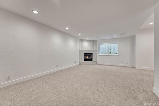 unfurnished living room with light colored carpet, baseboards, recessed lighting, and a glass covered fireplace