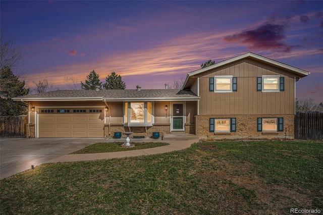 split level home with a lawn, driveway, fence, an attached garage, and brick siding