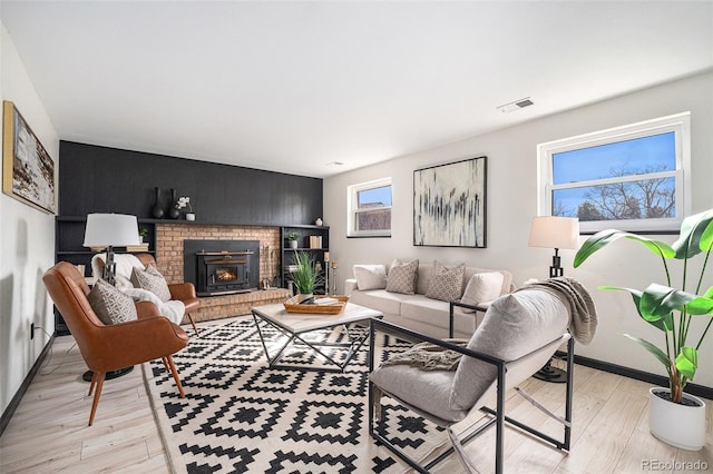 living room featuring visible vents, baseboards, a brick fireplace, and light wood finished floors