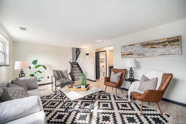 living area featuring stairs, light wood-style flooring, baseboards, and visible vents