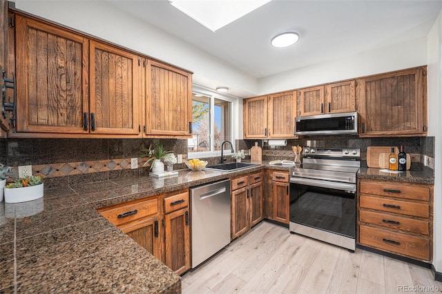 kitchen featuring a sink, tile counters, light wood-style floors, appliances with stainless steel finishes, and backsplash