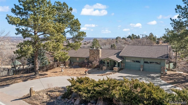 view of front of house featuring a tile roof, a chimney, concrete driveway, fence, and a garage