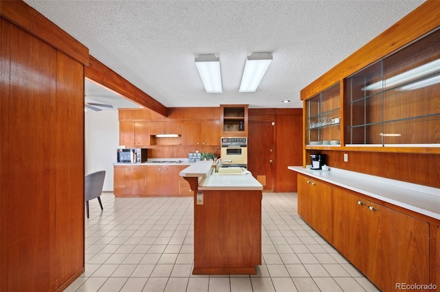 kitchen featuring white gas stovetop, a kitchen island with sink, light countertops, open shelves, and a sink