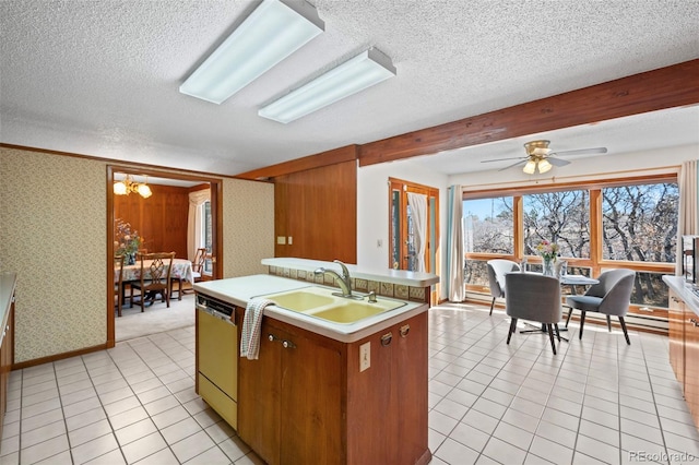 kitchen with a textured ceiling, dishwashing machine, light countertops, a center island with sink, and wallpapered walls