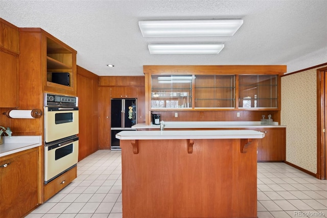 kitchen featuring double oven, light countertops, brown cabinets, open shelves, and wallpapered walls