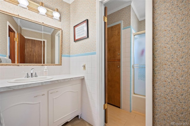 full bath featuring a wainscoted wall, vanity, tile walls, ornamental molding, and wallpapered walls