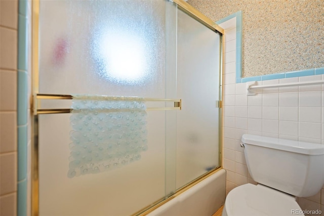 bathroom with toilet, a wainscoted wall, combined bath / shower with glass door, and tile walls