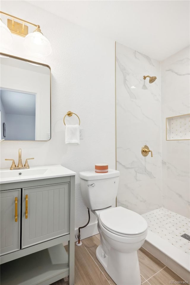 bathroom featuring hardwood / wood-style floors, toilet, a tile shower, and vanity