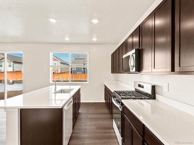 kitchen with dark brown cabinetry, appliances with stainless steel finishes, dark hardwood / wood-style flooring, an island with sink, and sink