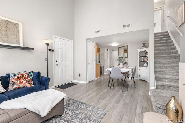 living room with light wood finished floors, baseboards, a towering ceiling, and stairs