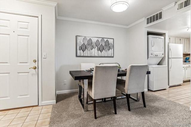 tiled dining area with stacked washer and clothes dryer and ornamental molding