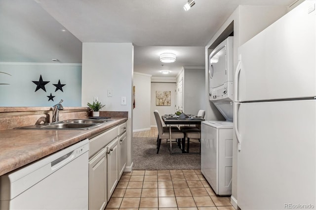 kitchen featuring sink, light tile patterned floors, stacked washer and dryer, white appliances, and white cabinets