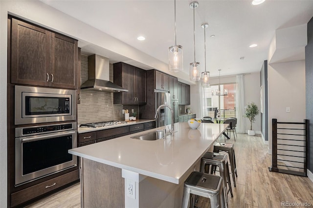 9072 E 47th Ave, Denver, CO 80238 - kitchen featuring appliances with stainless steel finishes, wall chimney range hood, a sink, a kitchen island with sink, and a breakfast bar area