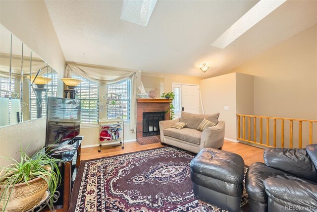 living area featuring baseboards, wood finished floors, vaulted ceiling with skylight, and a fireplace