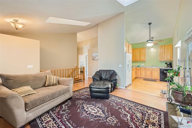 living room featuring a skylight, ceiling fan, high vaulted ceiling, and light wood-style floors