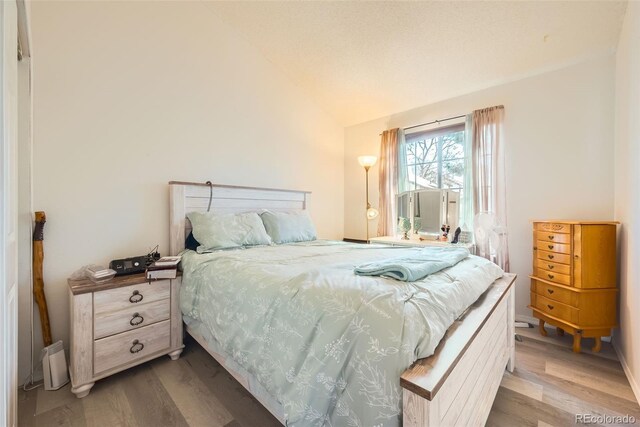 bedroom featuring baseboards, light wood finished floors, and vaulted ceiling