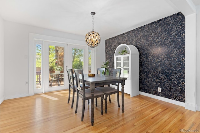 dining room with wallpapered walls, an accent wall, a chandelier, baseboards, and light wood-type flooring