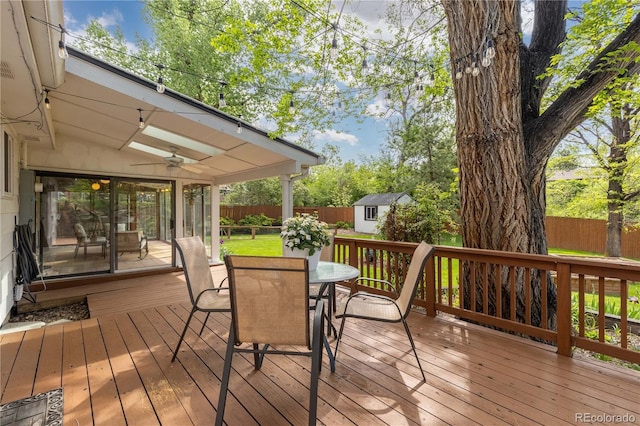 wooden terrace with outdoor dining area, a ceiling fan, a fenced backyard, an outbuilding, and a storage shed