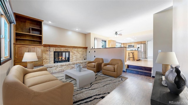 living area featuring a brick fireplace, ceiling fan, wood finished floors, and recessed lighting