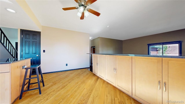 interior space featuring light brown cabinetry, light wood finished floors, a ceiling fan, and baseboards