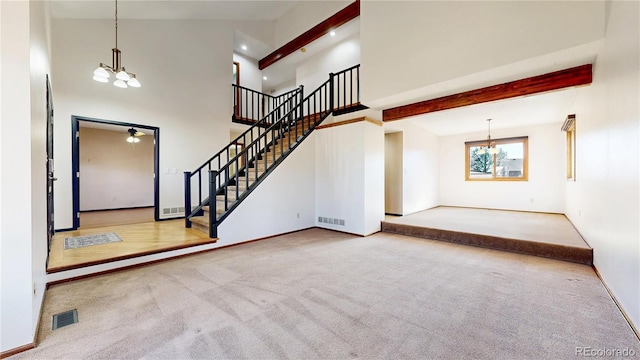 unfurnished living room with carpet, visible vents, a notable chandelier, and stairs