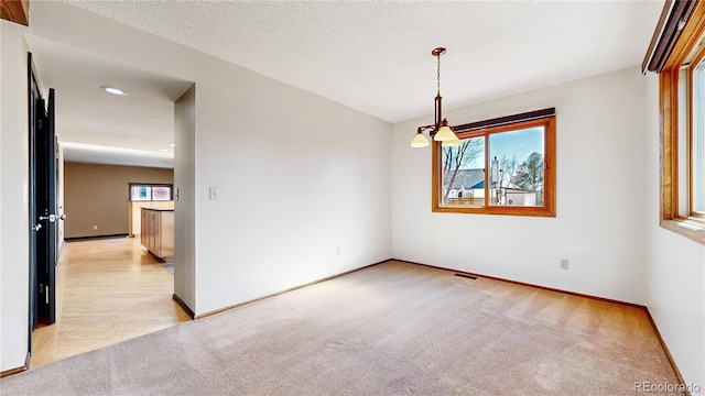 spare room featuring baseboards, a textured ceiling, visible vents, and light colored carpet