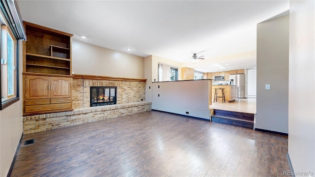 unfurnished living room featuring baseboards, visible vents, a ceiling fan, wood finished floors, and a fireplace