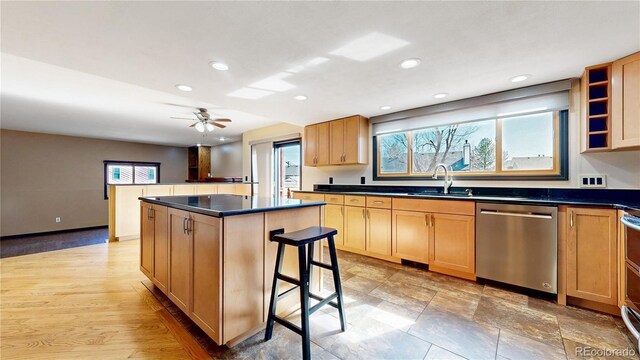 kitchen featuring dark countertops, a kitchen breakfast bar, a center island, stainless steel dishwasher, and a sink