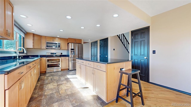 kitchen featuring dark countertops, a breakfast bar area, appliances with stainless steel finishes, a sink, and recessed lighting