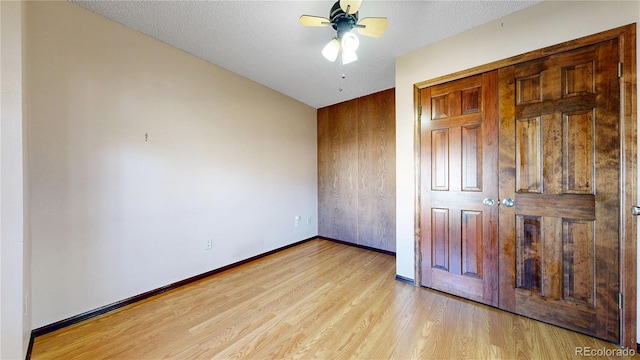 unfurnished bedroom featuring ceiling fan, a textured ceiling, baseboards, light wood-style floors, and a closet