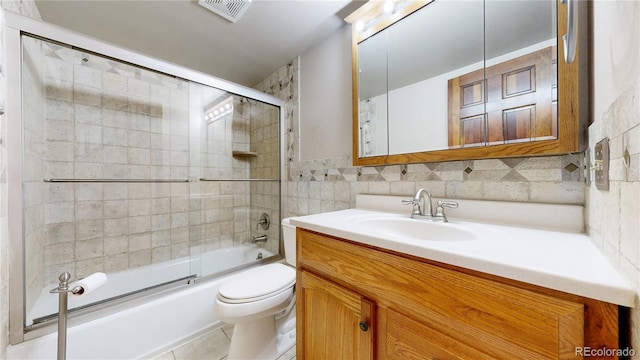 full bath featuring toilet, bath / shower combo with glass door, vanity, visible vents, and tile walls